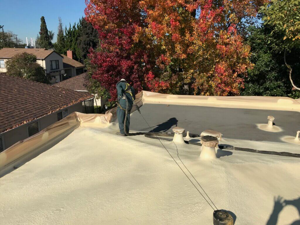 an Armstrong Foam Roofing technician spraying a flat foam roof with elastomeric recoating